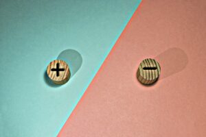 Wooden chips with a plus sign and a minus sign, on a blue and pink background. Representing pros and cons.